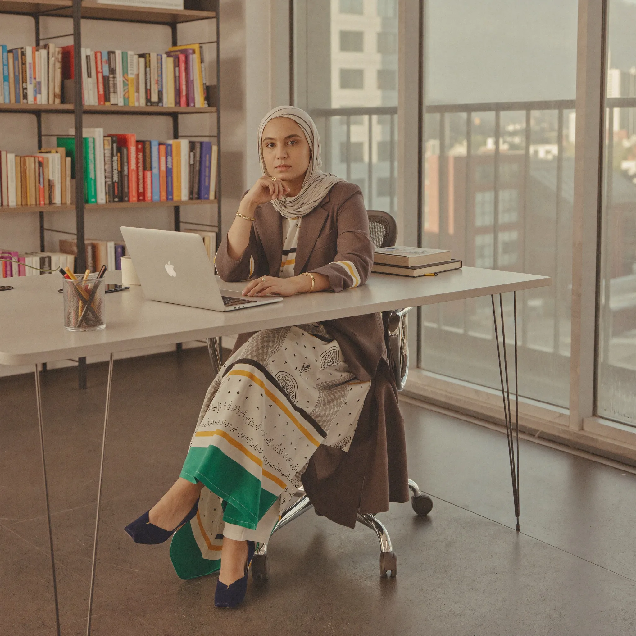 Humna Raza at her desk, laptop open, a wall of books behind her.